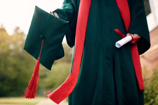 Seguros educativos; imagen de un joven recién graduado con su toga y su birrete en una mano mientras en la otra sostiene su diploma.